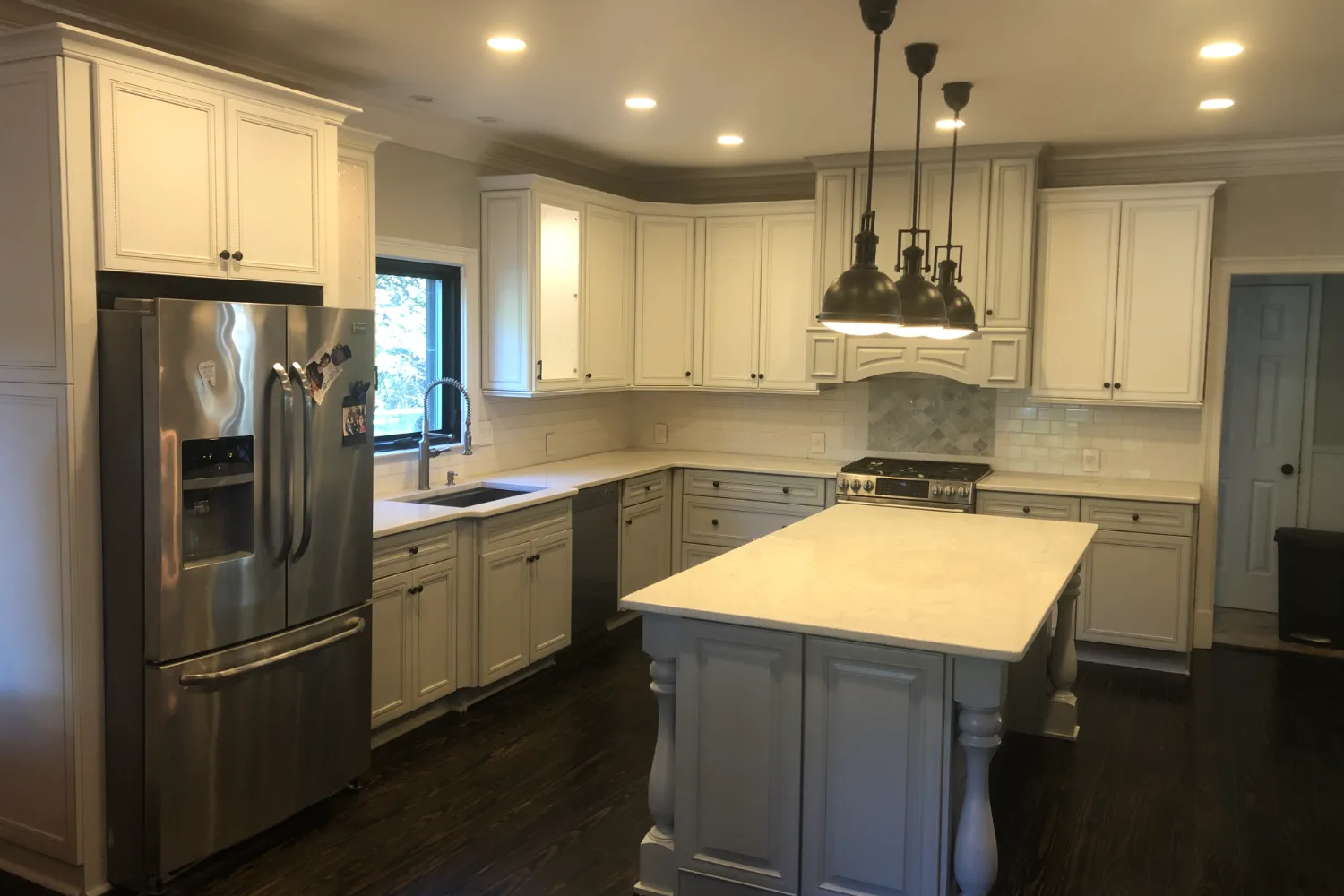 The same kitchen after refinishing, cabinets in white with a gray island