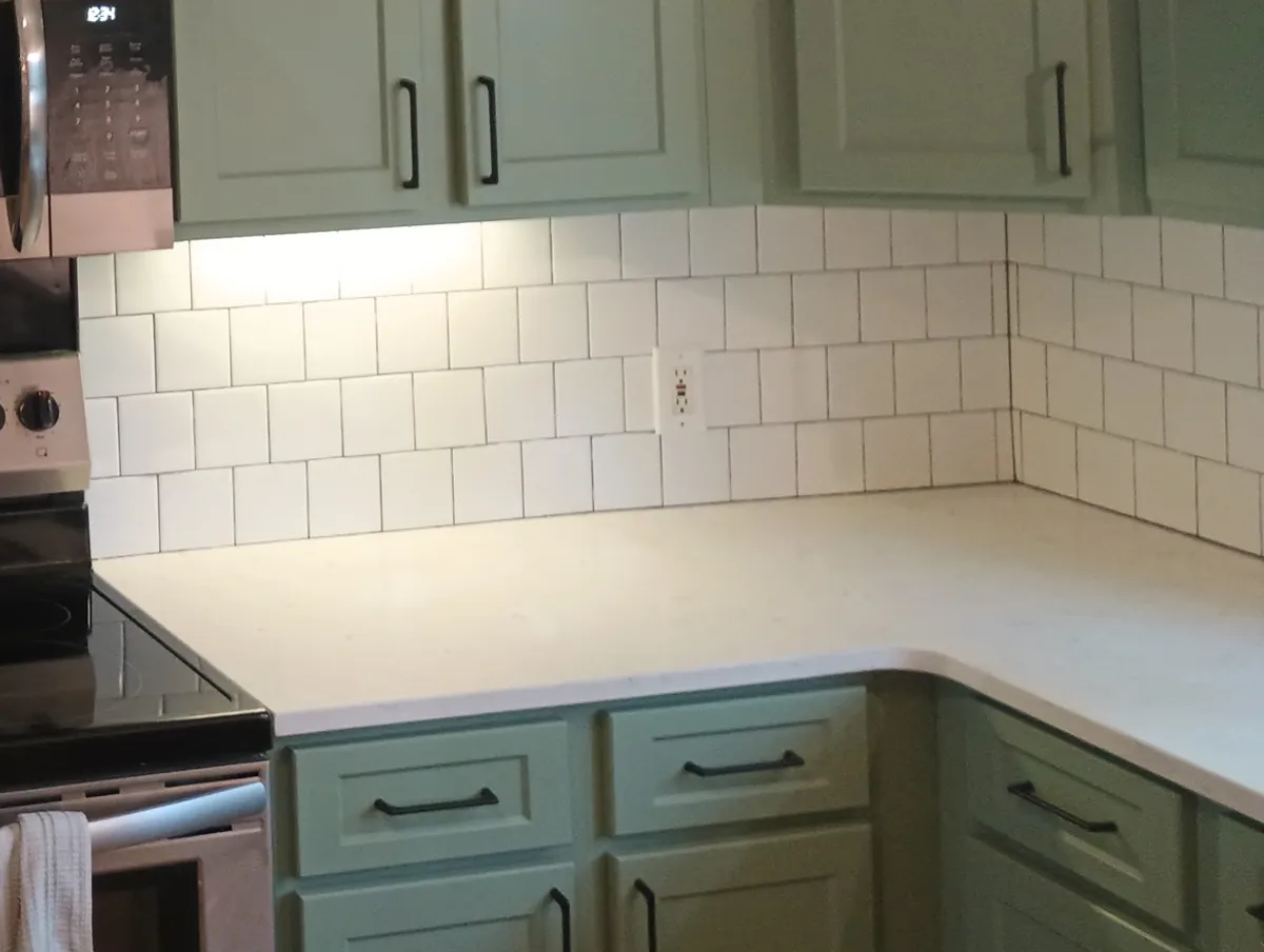 Sage green cabinets with white subway tile and black bar pulls