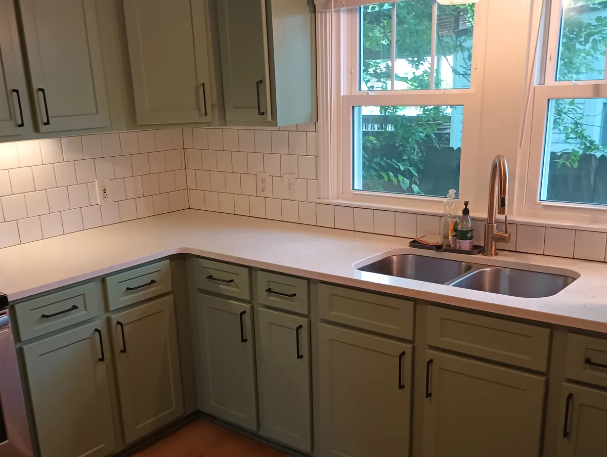 Sage green kitchen cabinets around a sink and window