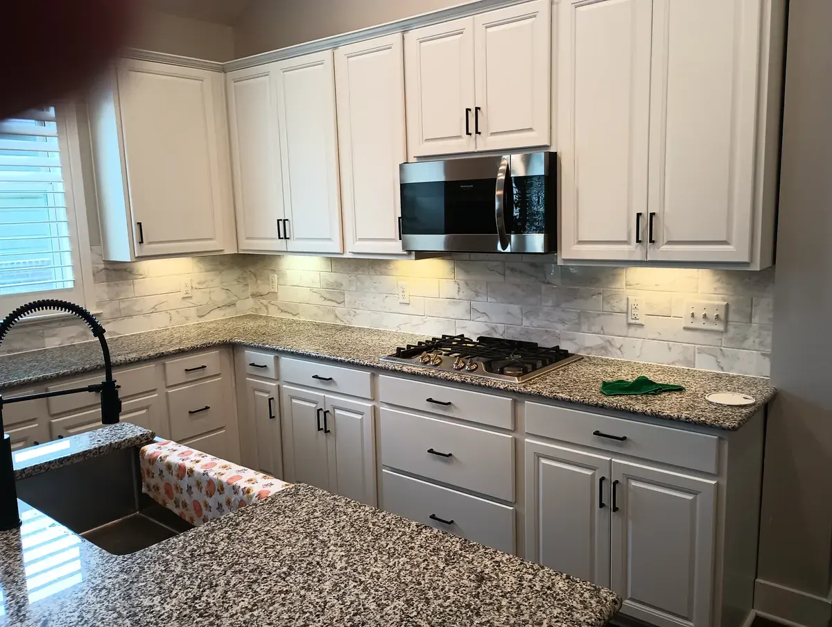 White refinished cabinets with granite counters and black hardware
