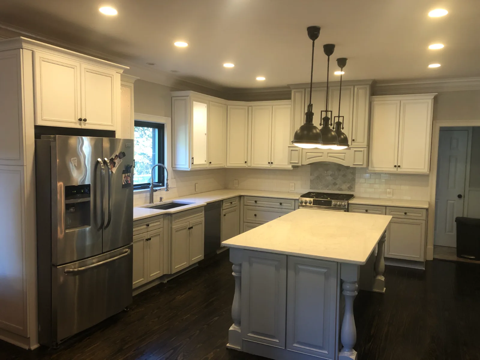 Restored white kitchen cabinets with a gray island, pendant lights, and dark wood floors